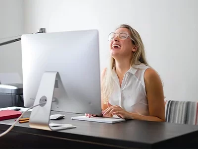 Mulher sorridente à frente de um computador, estando a frequentar o ensino à distância