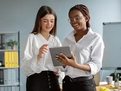 Duas mulheres no escritório usando um tablet para trabalho. Esta imagem representa a importância dos estágios na formação profissional inicial.